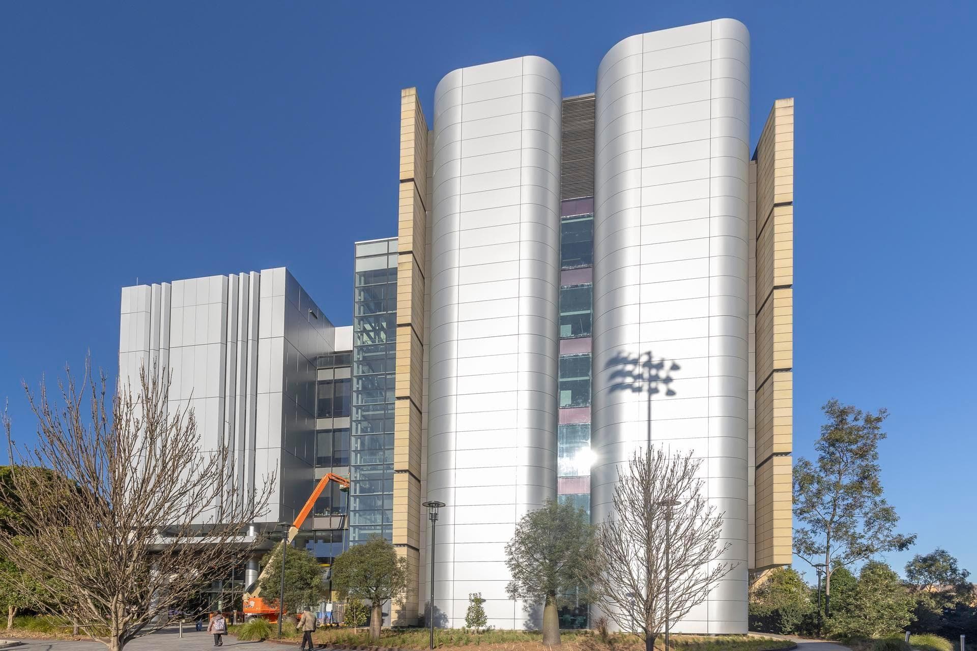 Front view of the Charles Perkins Centre with Alpolic NC curved silver panels and beige cladding framing the central glass atrium.