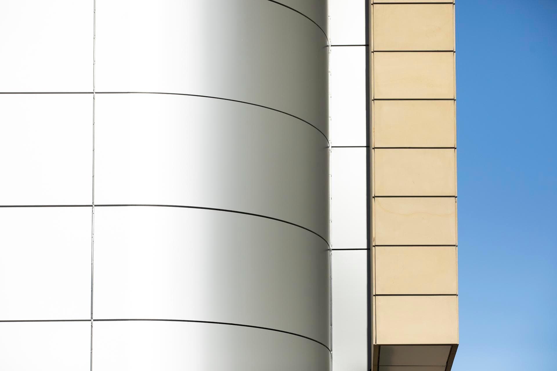 Detailed architectural shot of curved Alpolic NC silver panels meeting beige rectangular cladding at the Charles Perkins Centre.