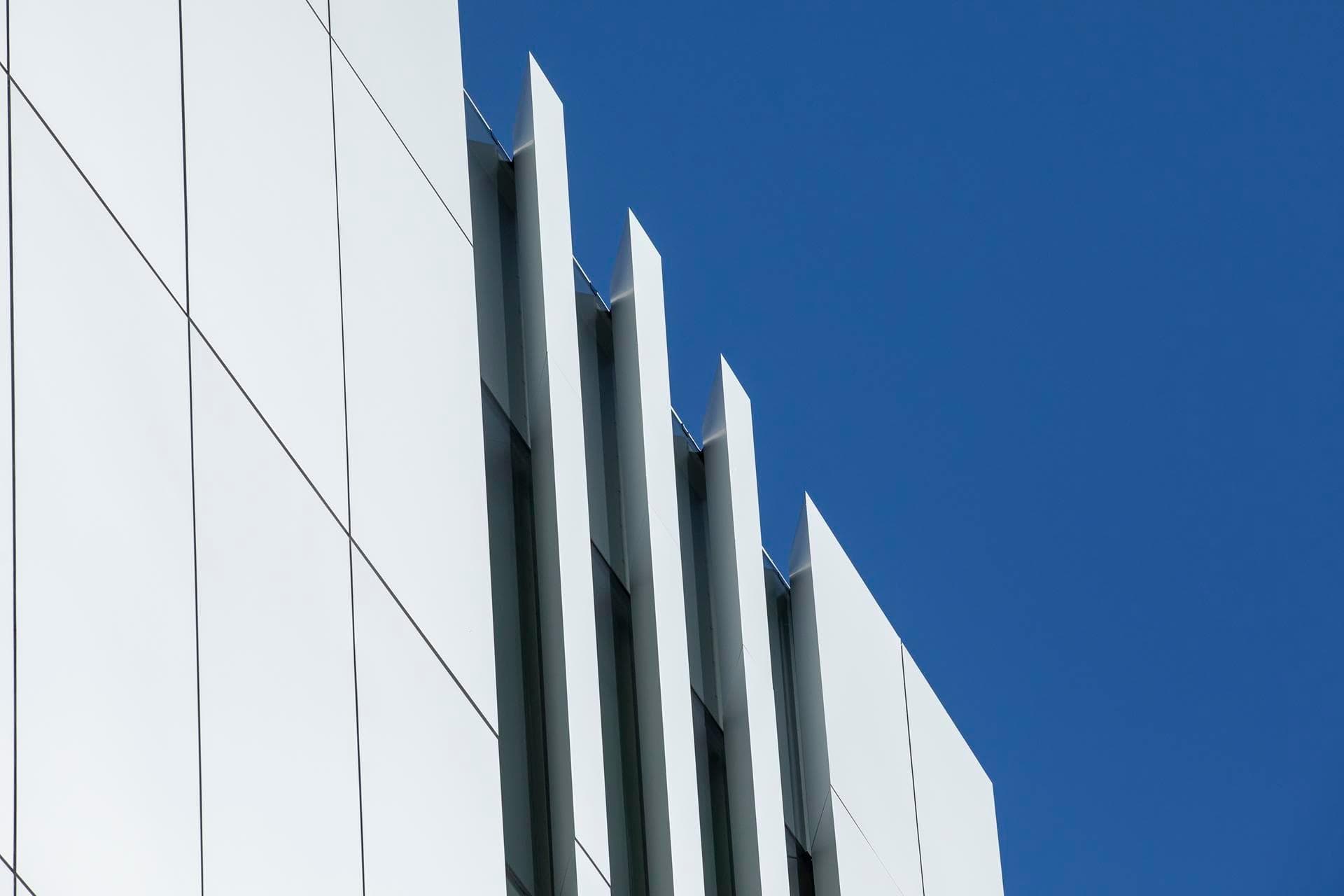 Upper façade of the Charles Perkins Centre showing Alpolic NC vertical fins and smooth white cladding against a clear blue sky.